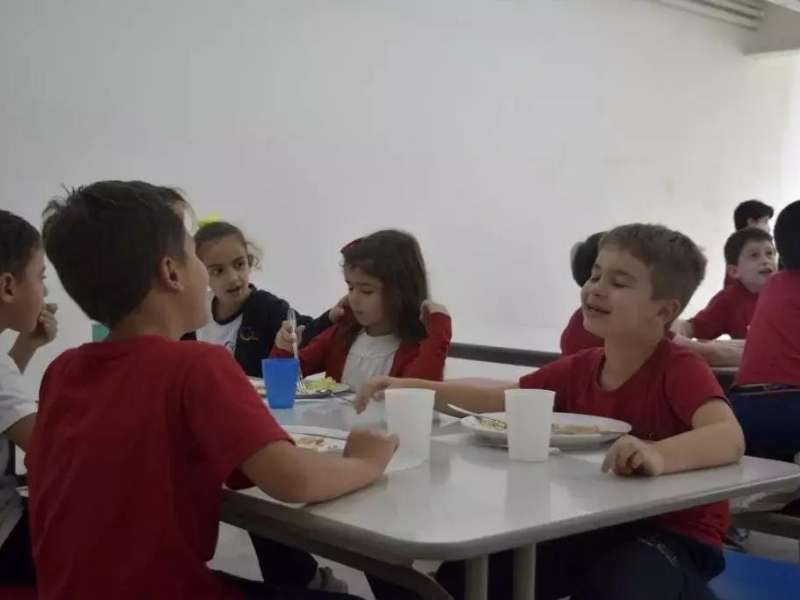 Crianças comendo em grupo no refeitório da escola Cycle.