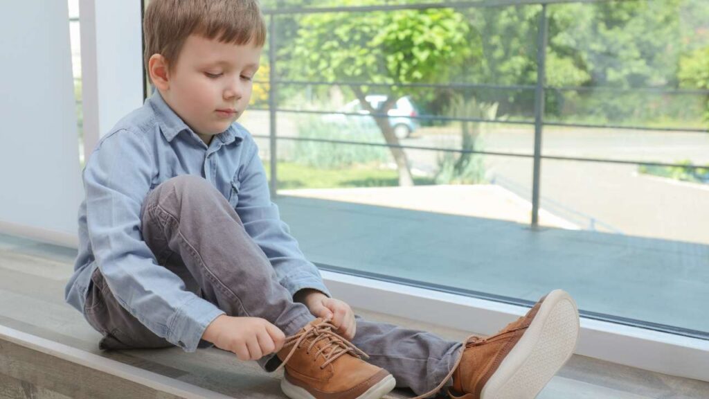 Menino amarrando sapato sozinho aprendendo a ter autonomia.